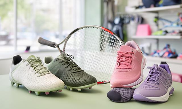 Voetbalschoenen, tennisracket en hardloopaccessoires naast elkaar in een lichte sportwinkel